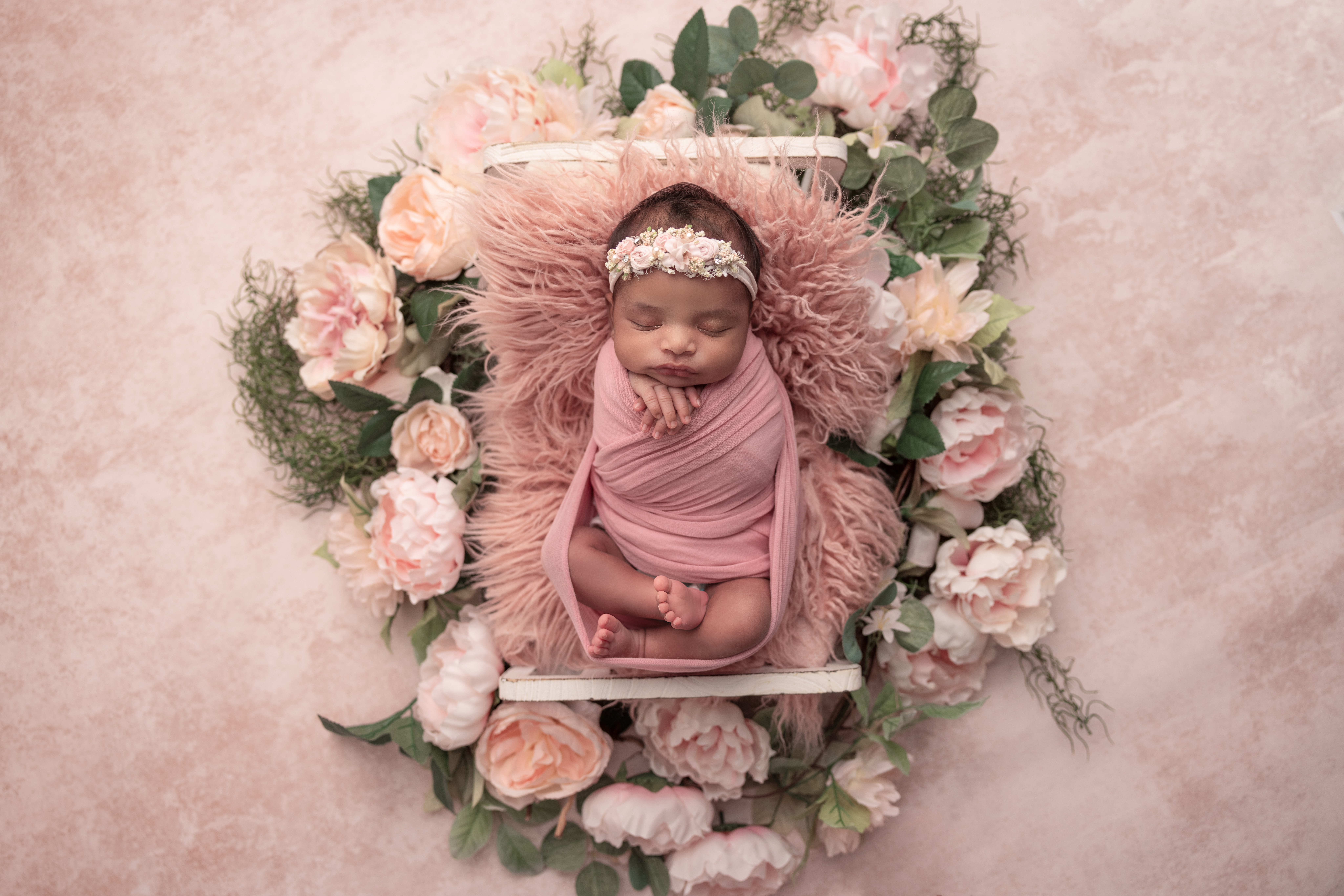 Baby girl wrapped in pink lying on a baby bed with beautiful florals around the bed