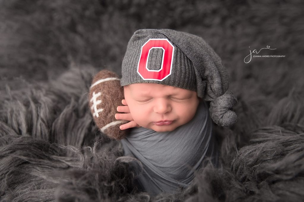 Newborn Baby Boy wrapped in Gray with a Buckeye Hat holding a football