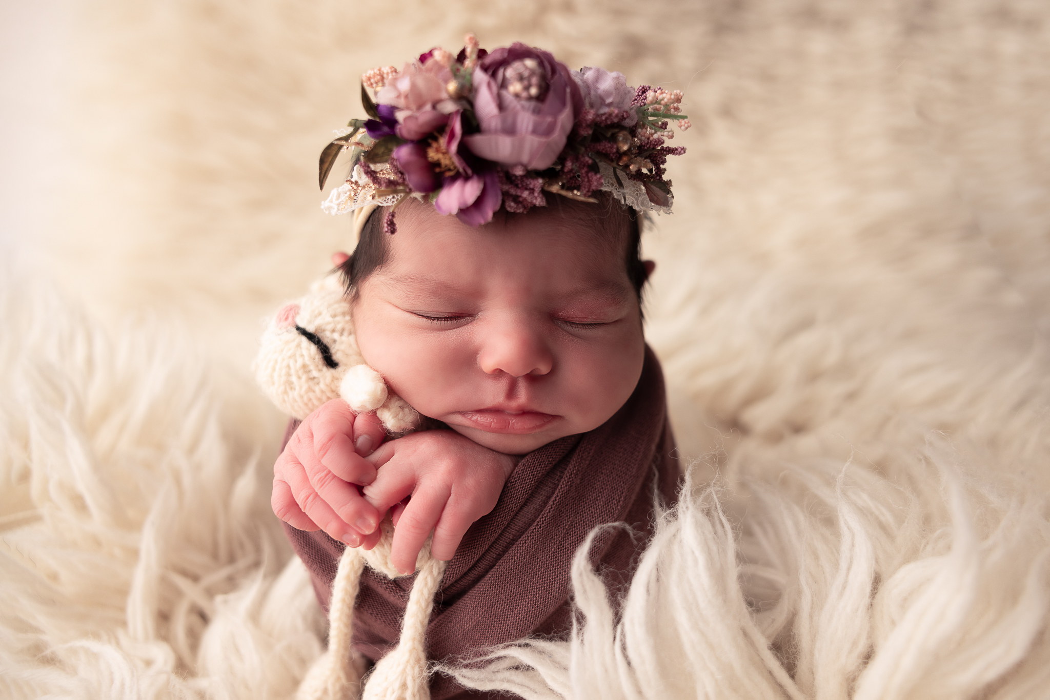 Baby wrapped in purple with floral headband holding lovey