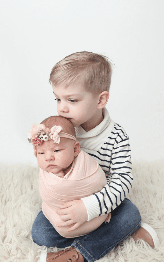 Little boy holding and kissing his baby sister in pink