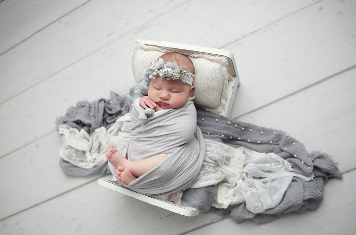 Little girl in grey blankets with headband in white bassinet