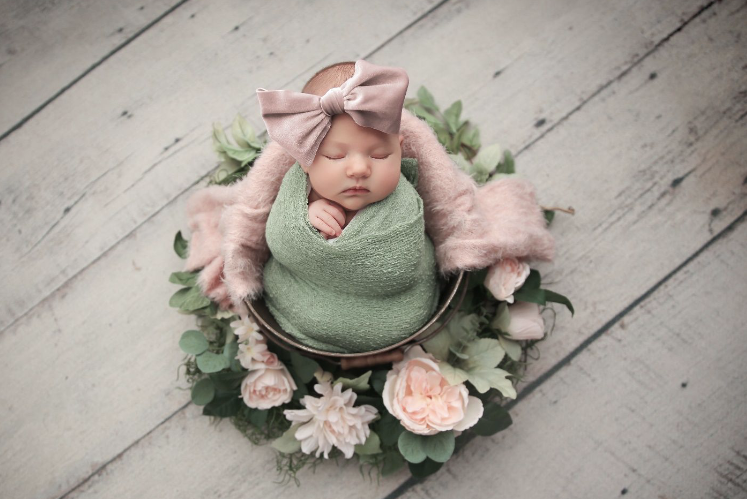 Baby girl in pink blow and green blanket surrounded by flowers