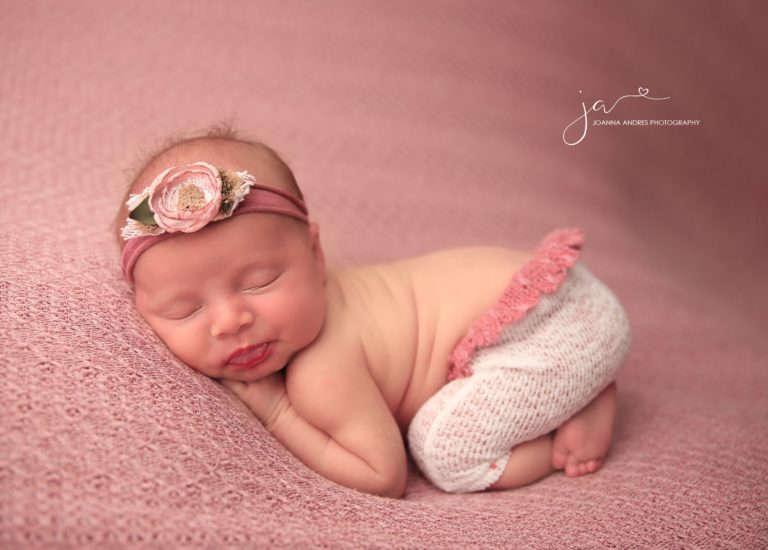 Baby with flower headband sleeping on pink blanket.