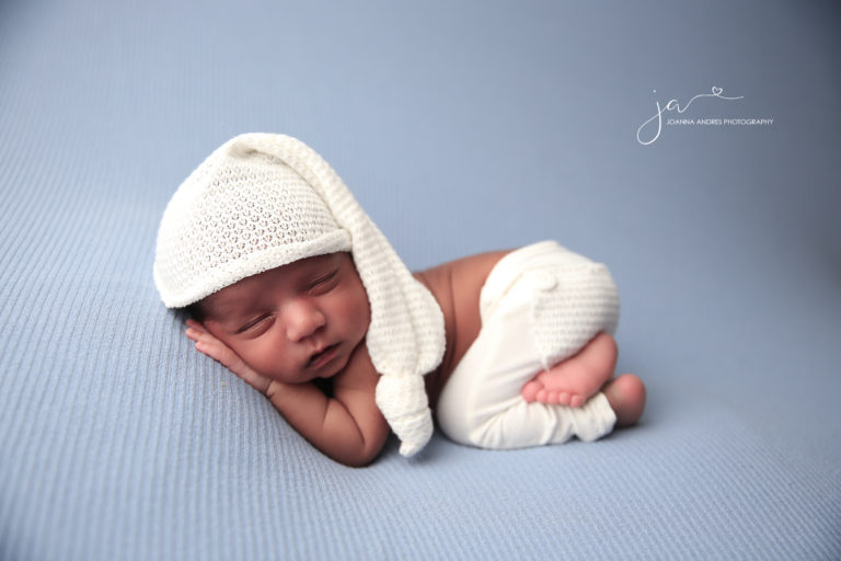 Baby boy with knitted cream colored hat sleeping on blue blanket.