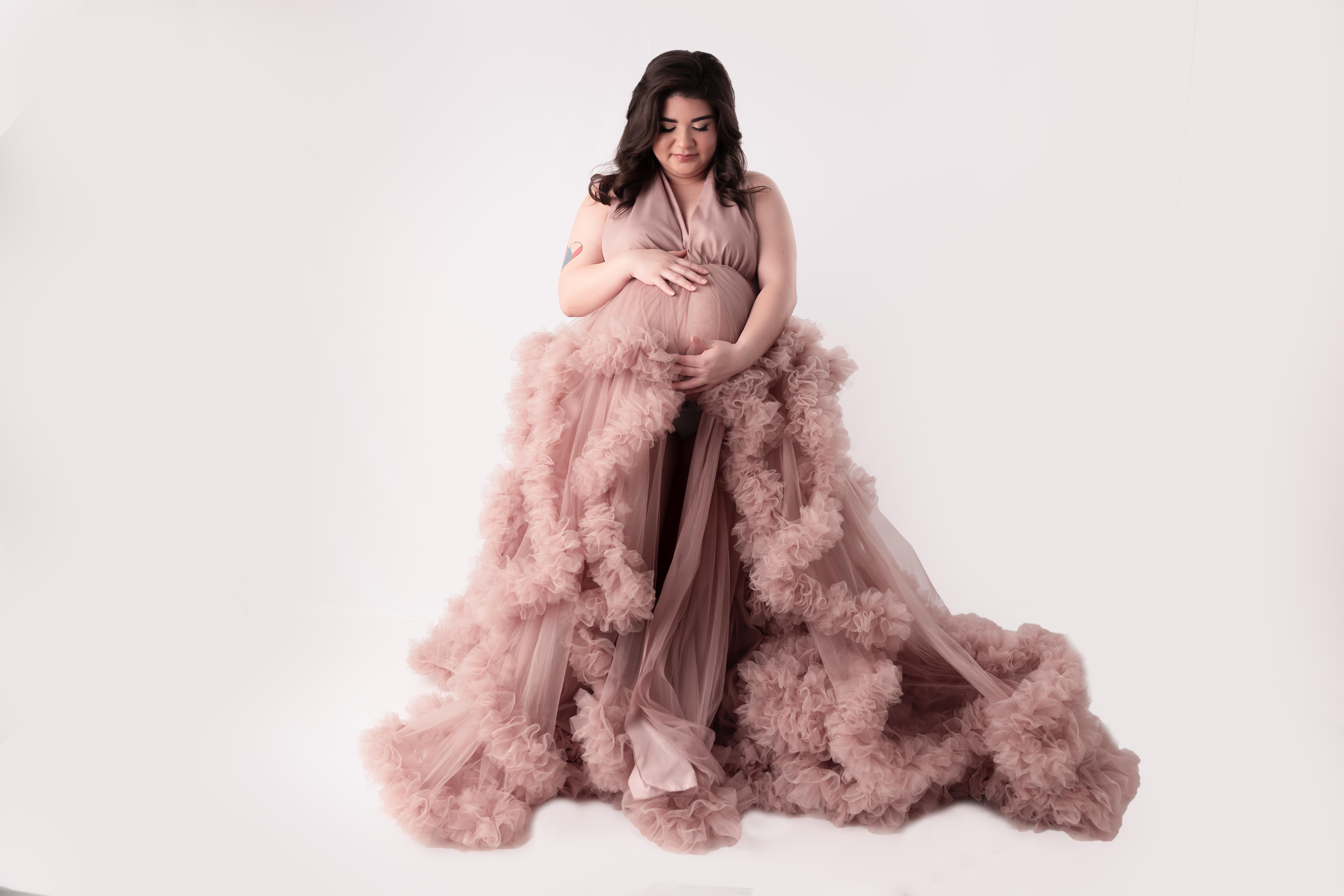 Woman wearing a beautiful pink maternity gown holding her pregnant bare bally