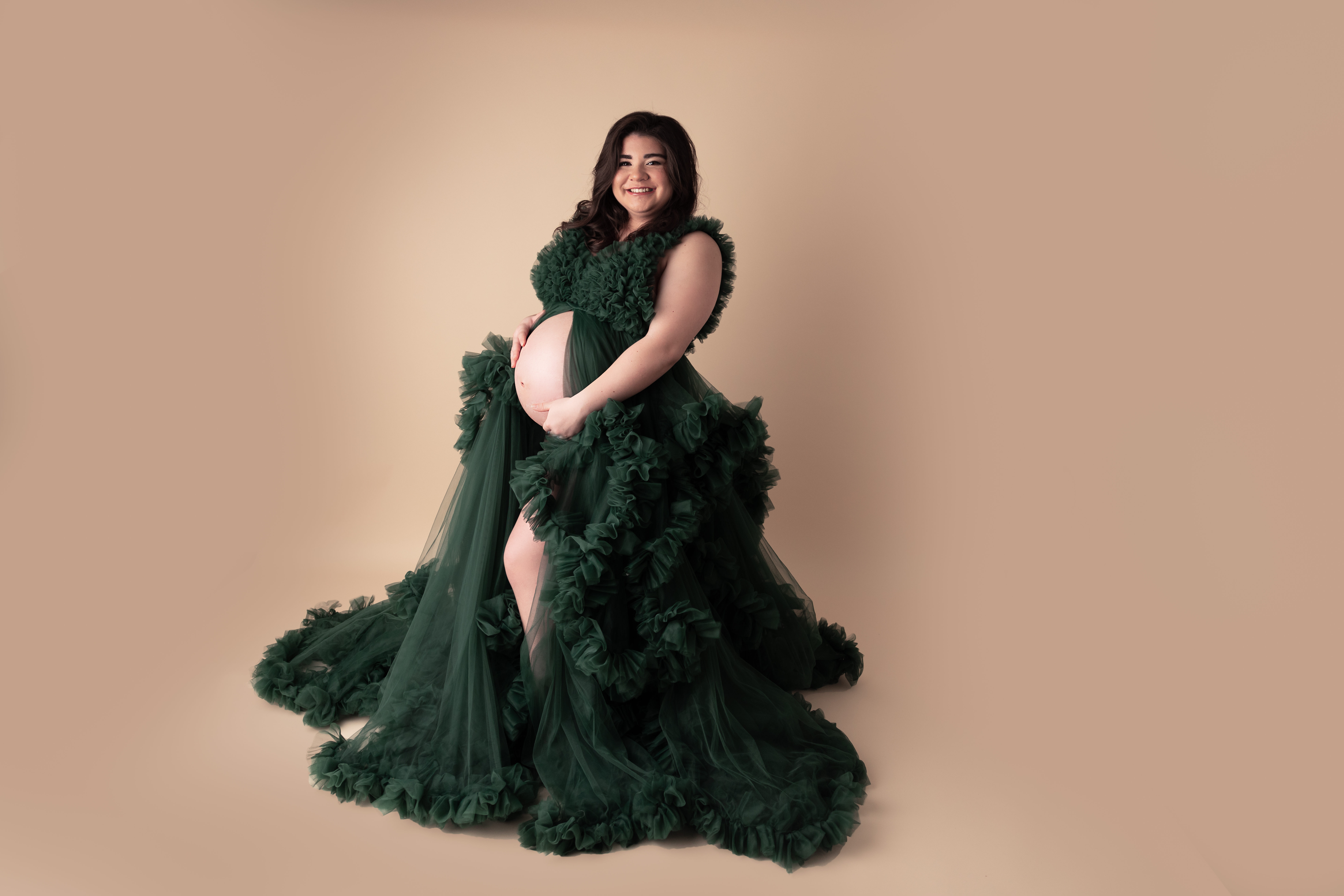 Woman wearing a big green tulle gown with belly exposed holding her pregnant belly