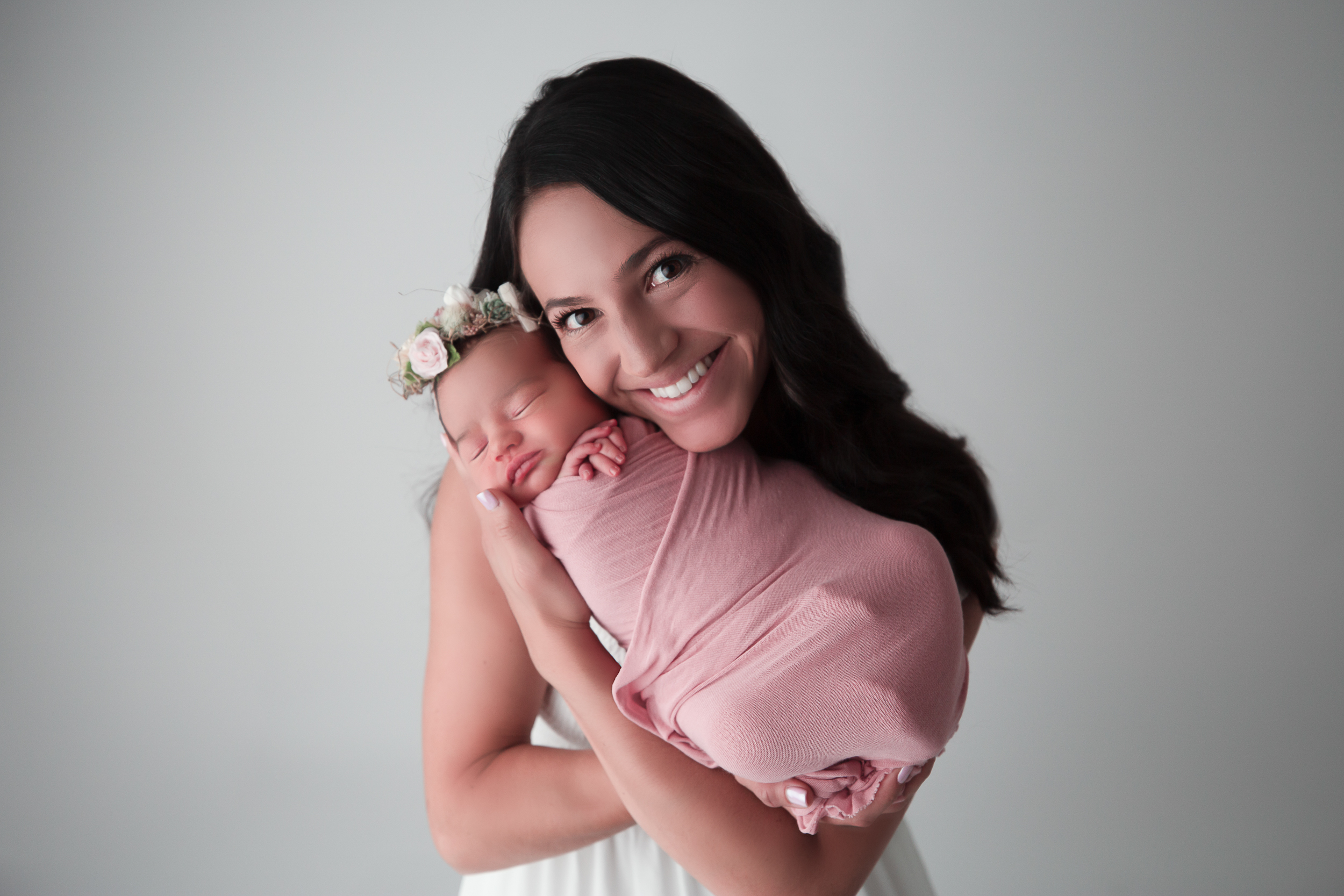 Bruneete Mother holding her baby who is wrapped in a pink swaddle and floral headband