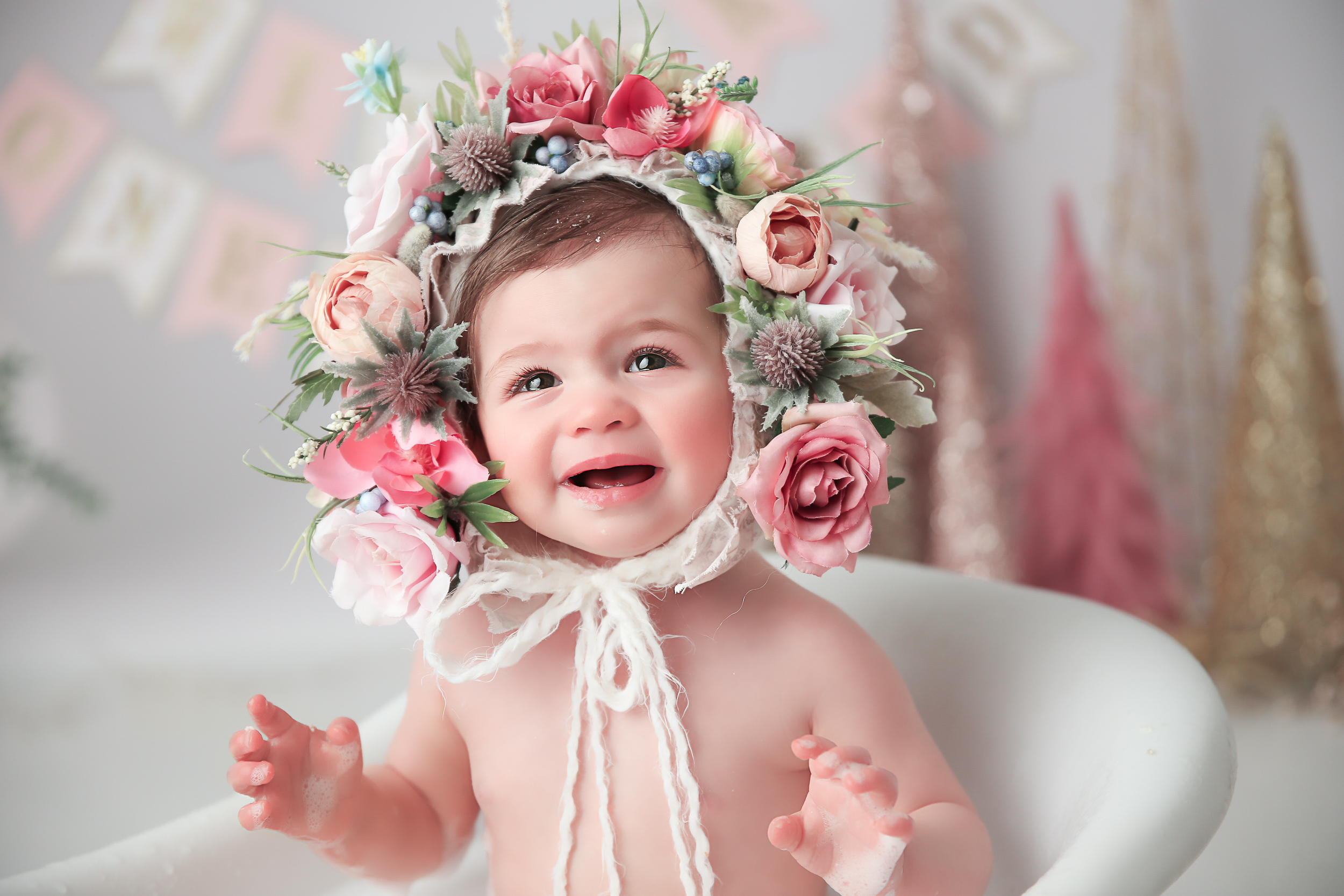 close up of a baby girl in a floral bonnet smiling while she's in a bathrub