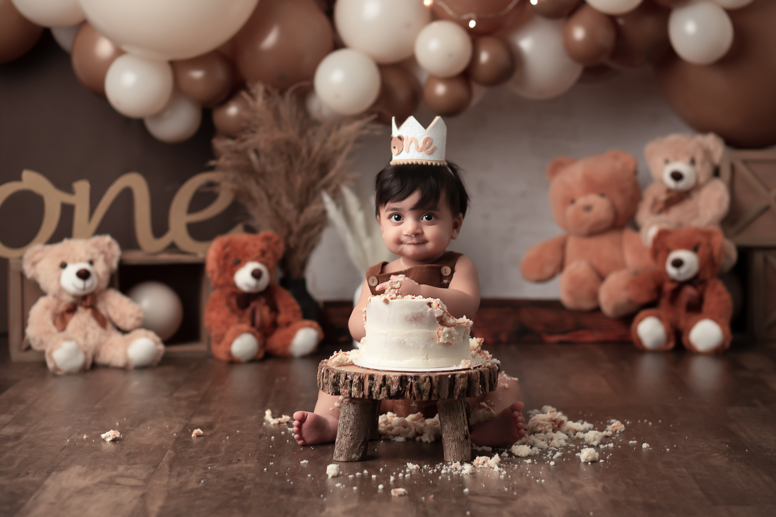 Cake Smash Session of a baby wearing a crown and teddy bears in the backdrop with balloon banner in browns and creams