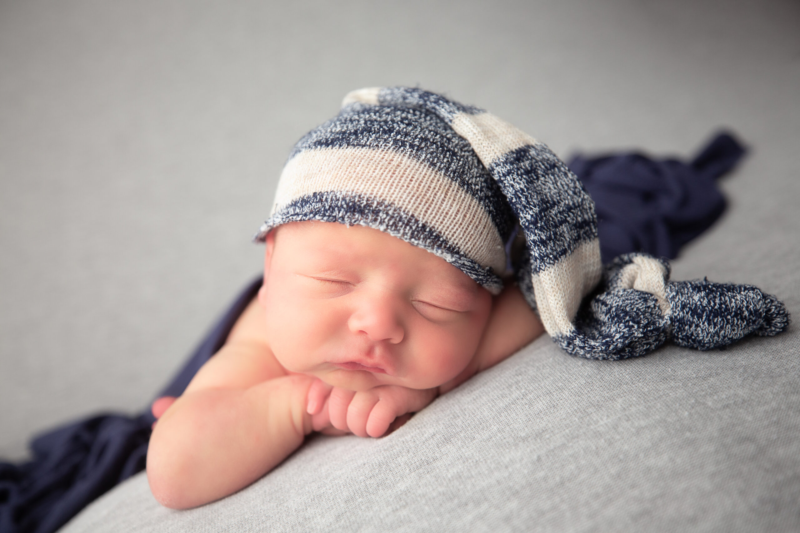 Baby boy with blue and white had posed with hands folded under his chin