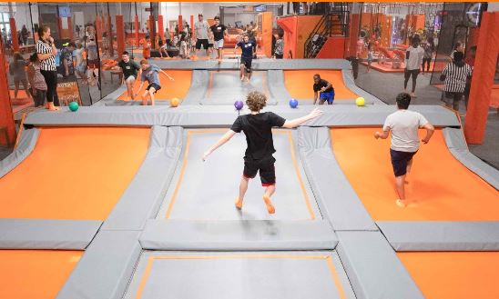 A boy in a black T-shirt and shorts jumping on a trampoline in a big trampoline park