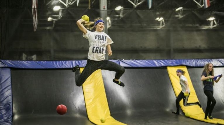 A teenage girl with a purple bandana on her head jumping on a trampoline holding a ball