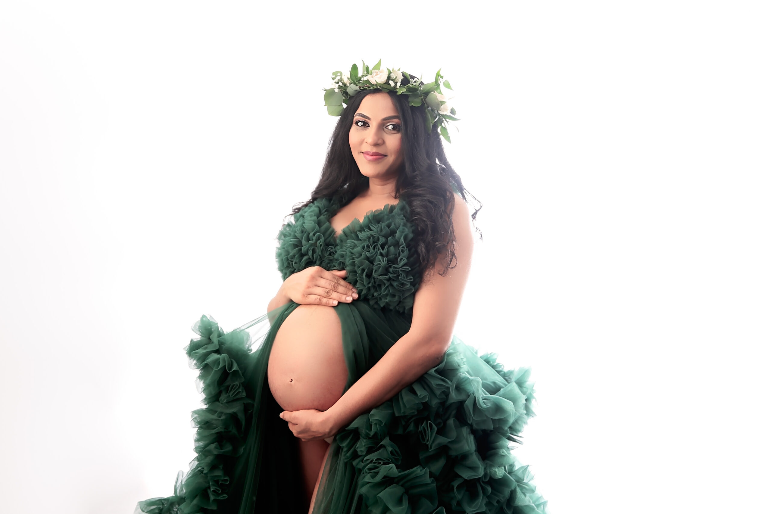 Pregnant woman with floral crown and black hair wearing a green maternity gown