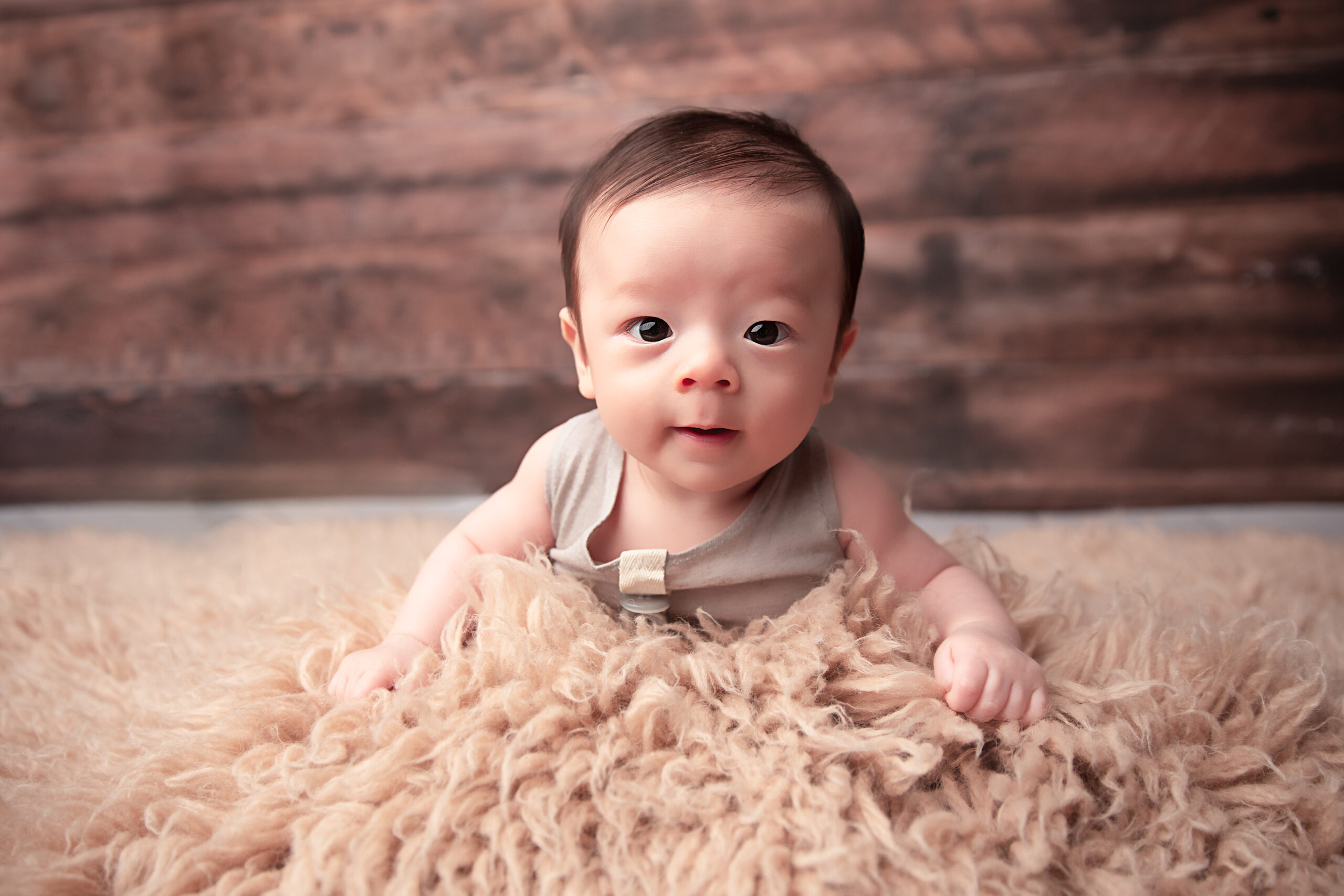Baby Boy laying on belly wearing a neutral outfit and wood backdrop