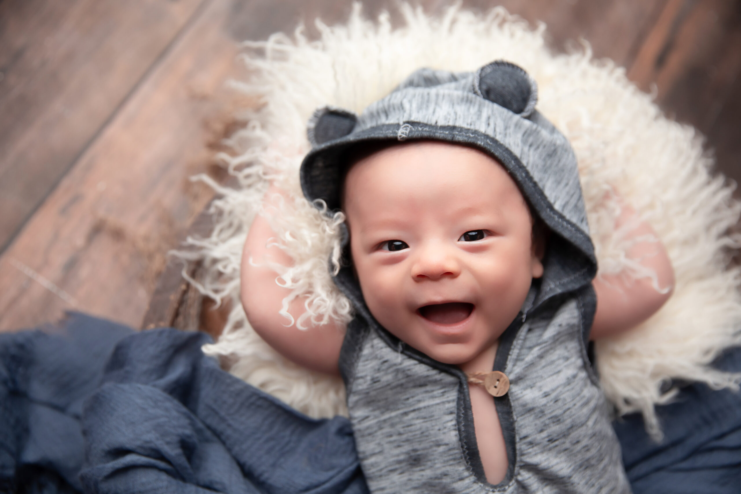 Baby smiling wearing a blue outfit with a hood with ears on them.