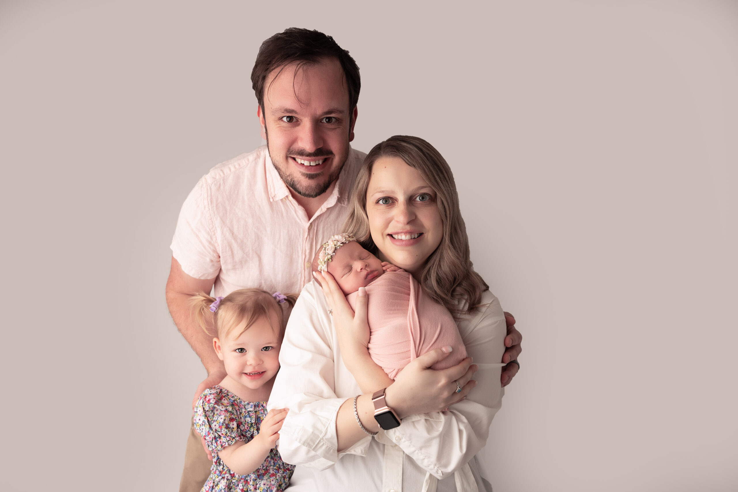 Family Portrait including mom, dad, older sibling girl in pigtails and newborn baby wrapped in pink