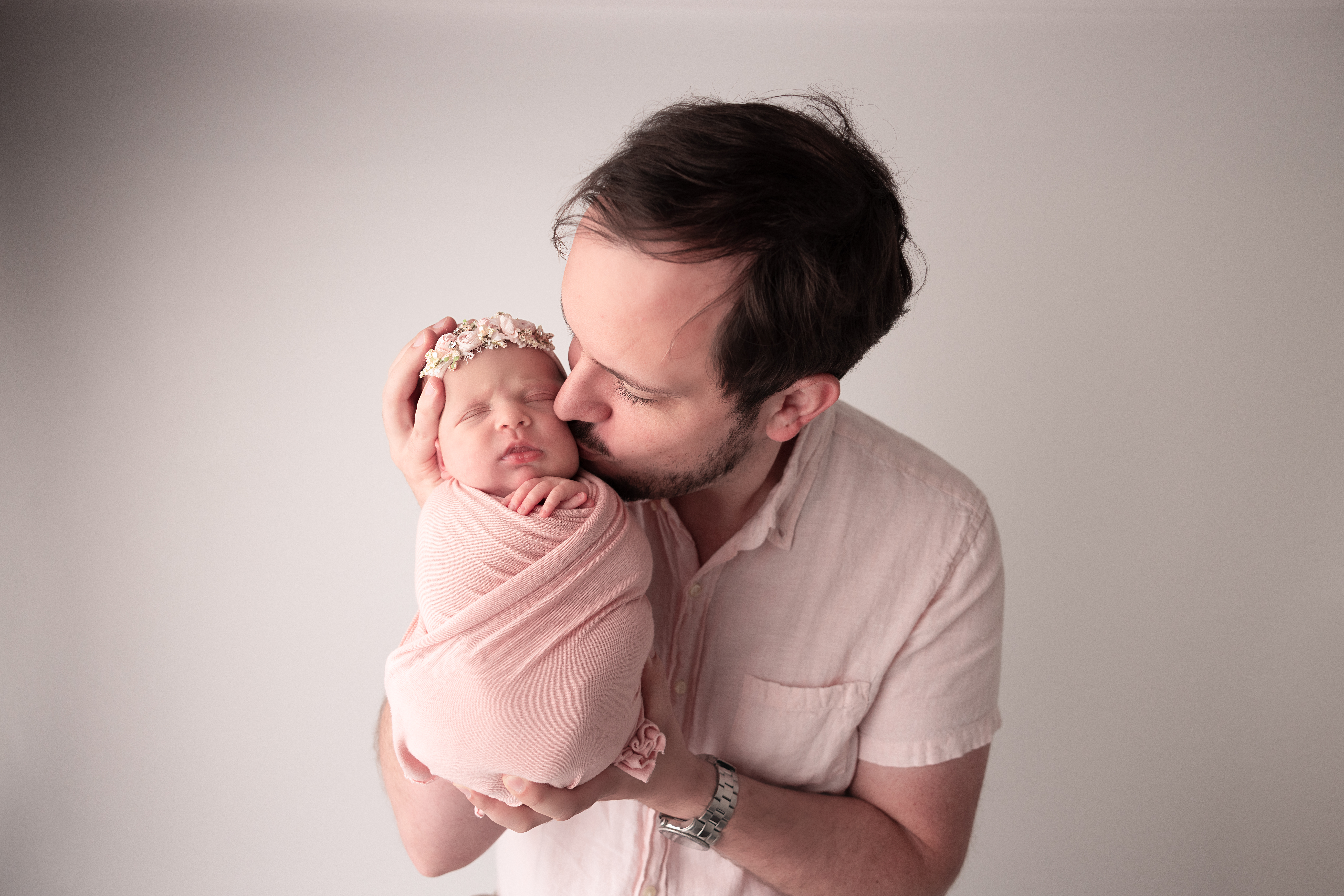 Dad kissing his newborn baby girl wrapped in pink with a headband