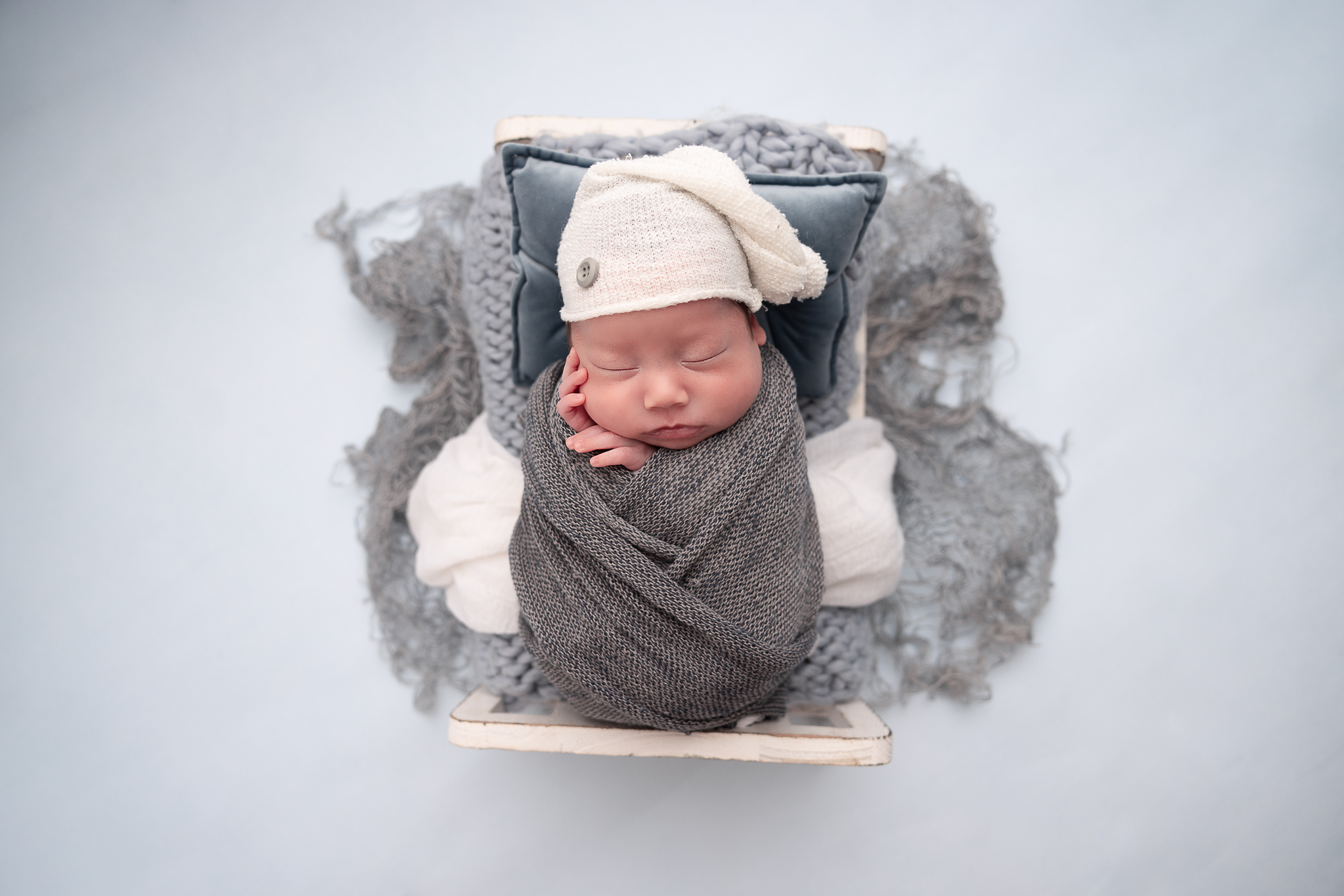 Newborn Baby in a blue wrap with one hand on his cheek, laying in a bed with layers