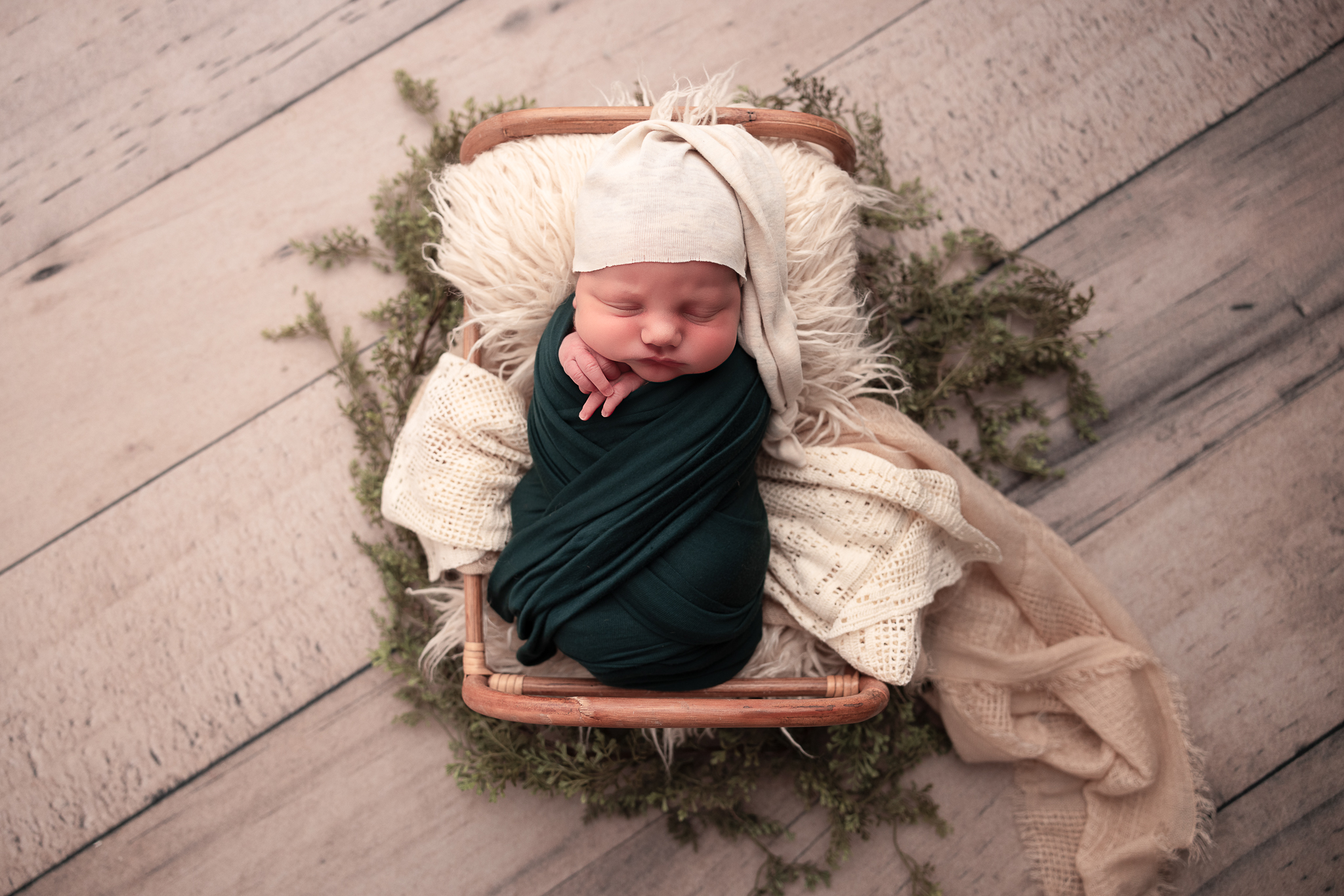 newborn baby boy in a prop and greenery wrapped in a forest green swaddle wearing a hat