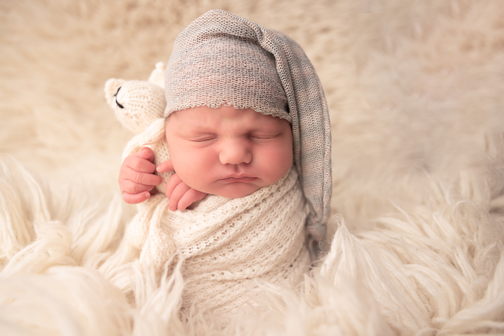 Baby Swaddled and holding a lovey wearing a light green hat