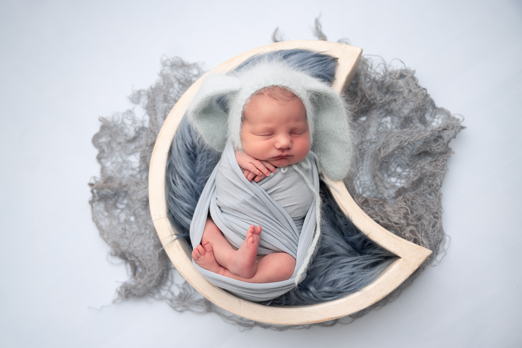 Baby in a moon prop wrapped with blue bonnet and with blue layers