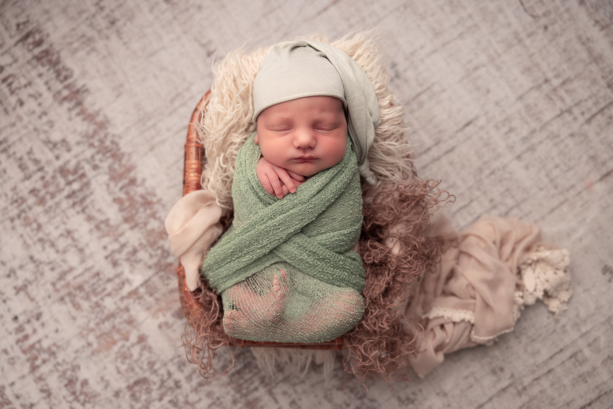 Baby laying in a prop wrapped in a green swaddle and wearing a hat