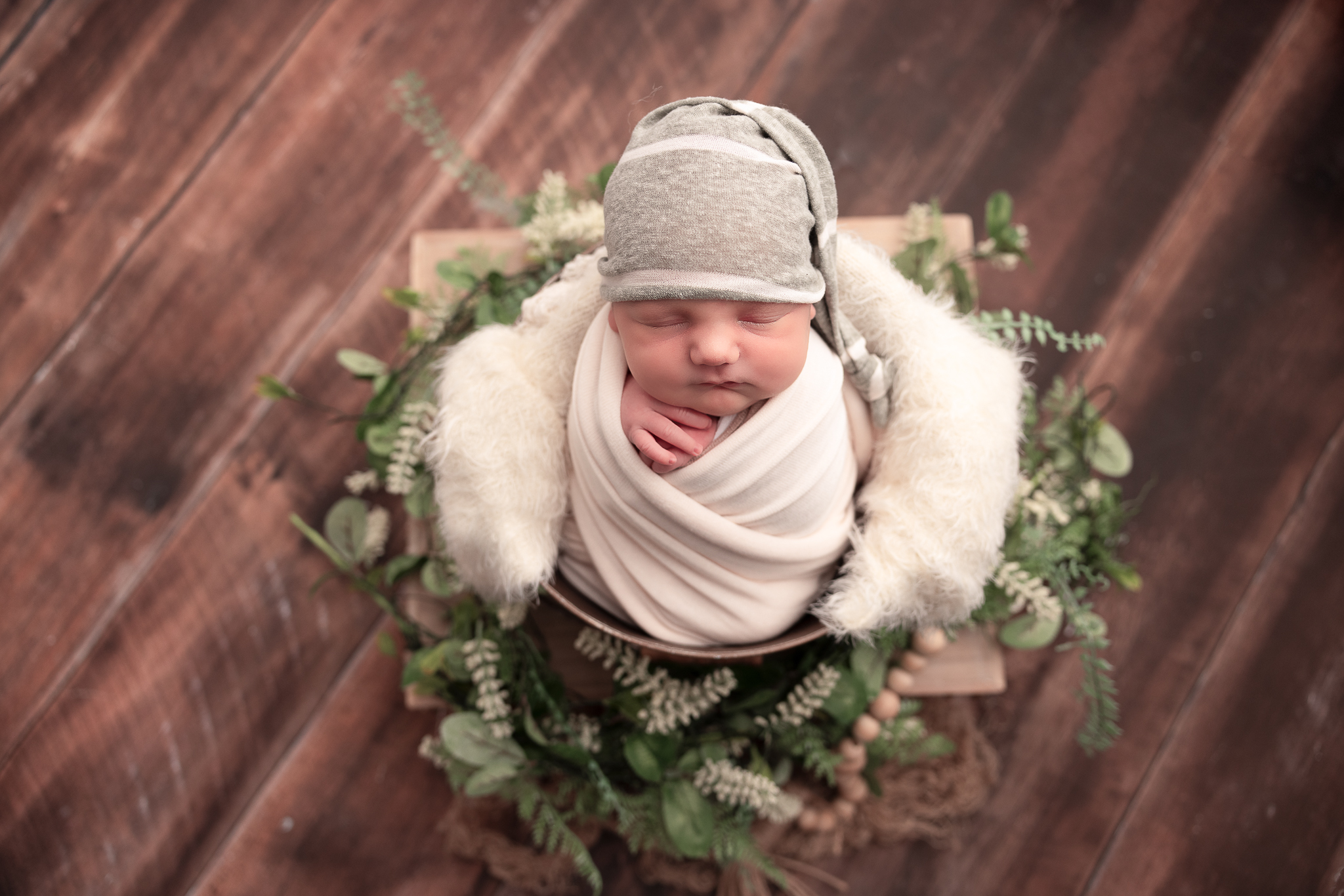 Baby in a bucket swaddled in cream and wearing a light green and white striped hat