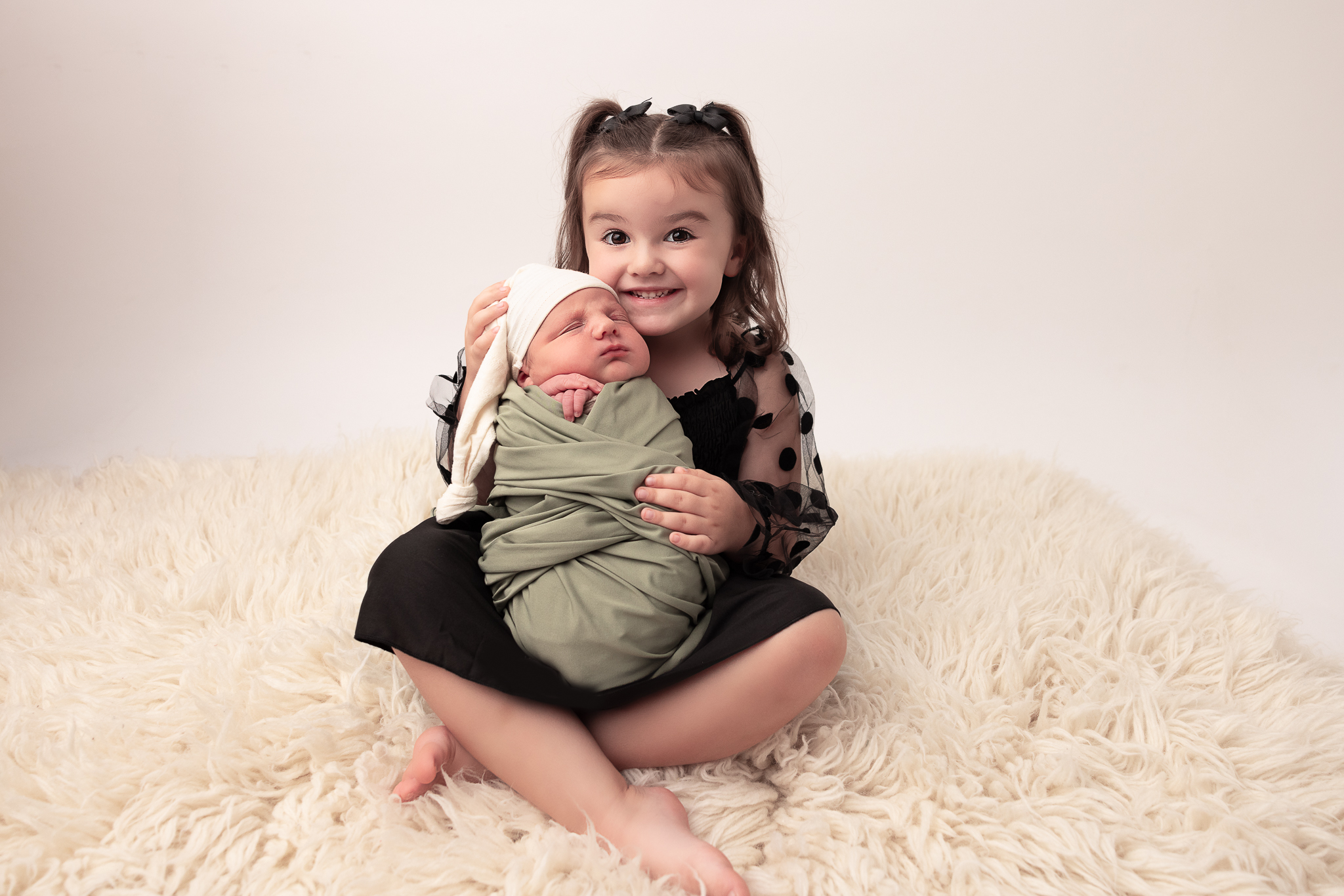 Big Sister sitting and holding her baby brother proudly