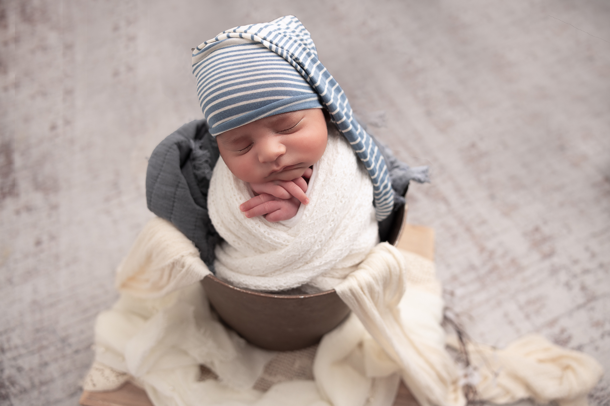 Baby in a bucket wrapped in white with a blue and white striped hat