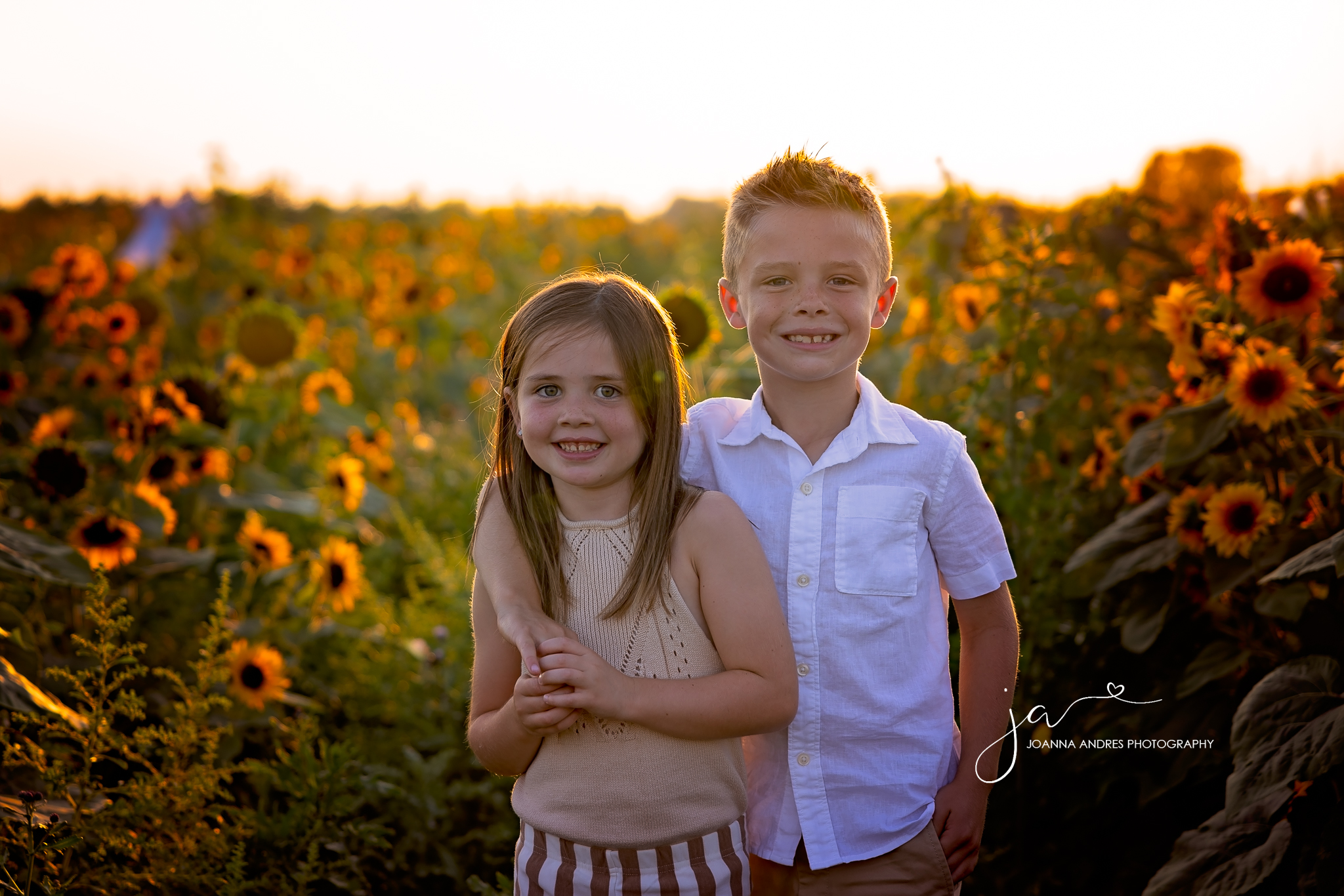 Silbings smiling and looking at the camera in the middle of a sunflower field