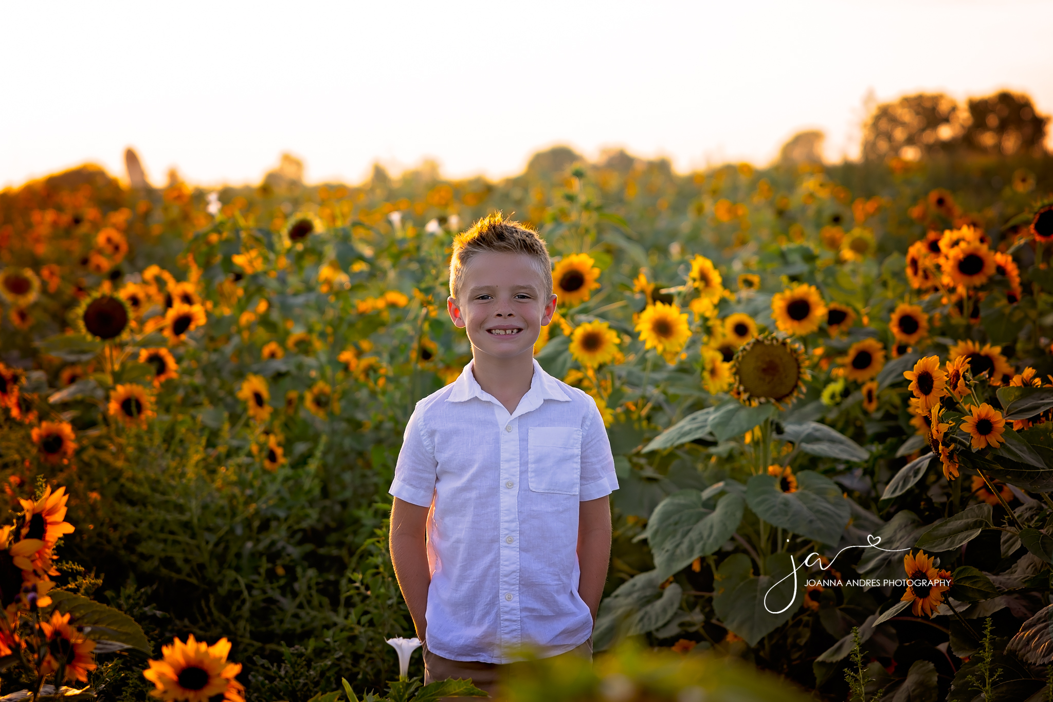 boy looking at the camera and smiling in the middle of a sunflower field