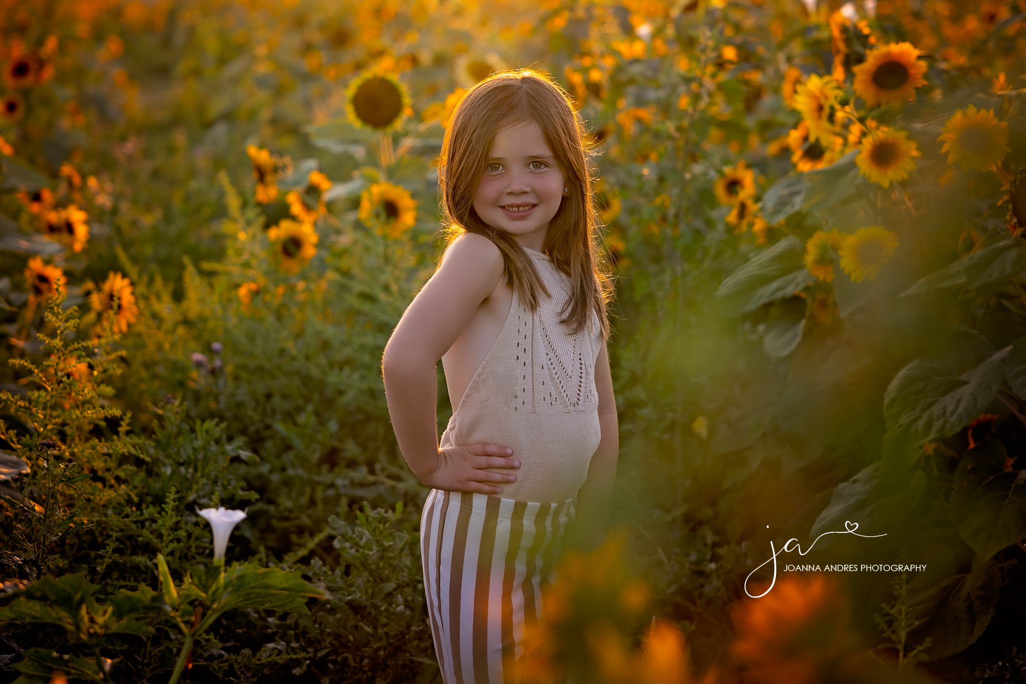 Girl with hand on hips and striped pants in the middle of a sunflower field at lynds fruit farm