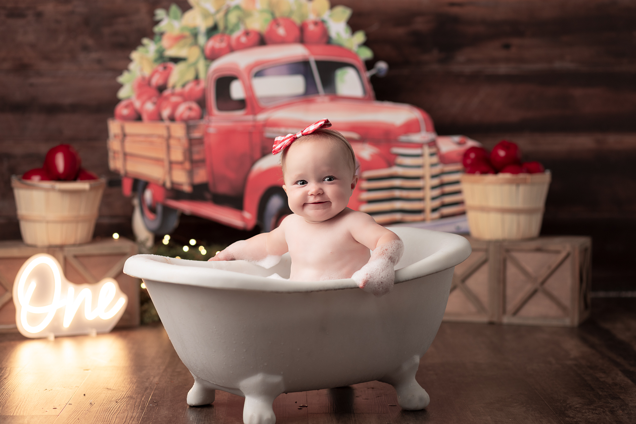 Baby in a Bathtub with a Red Truck full of apples in the backdrop