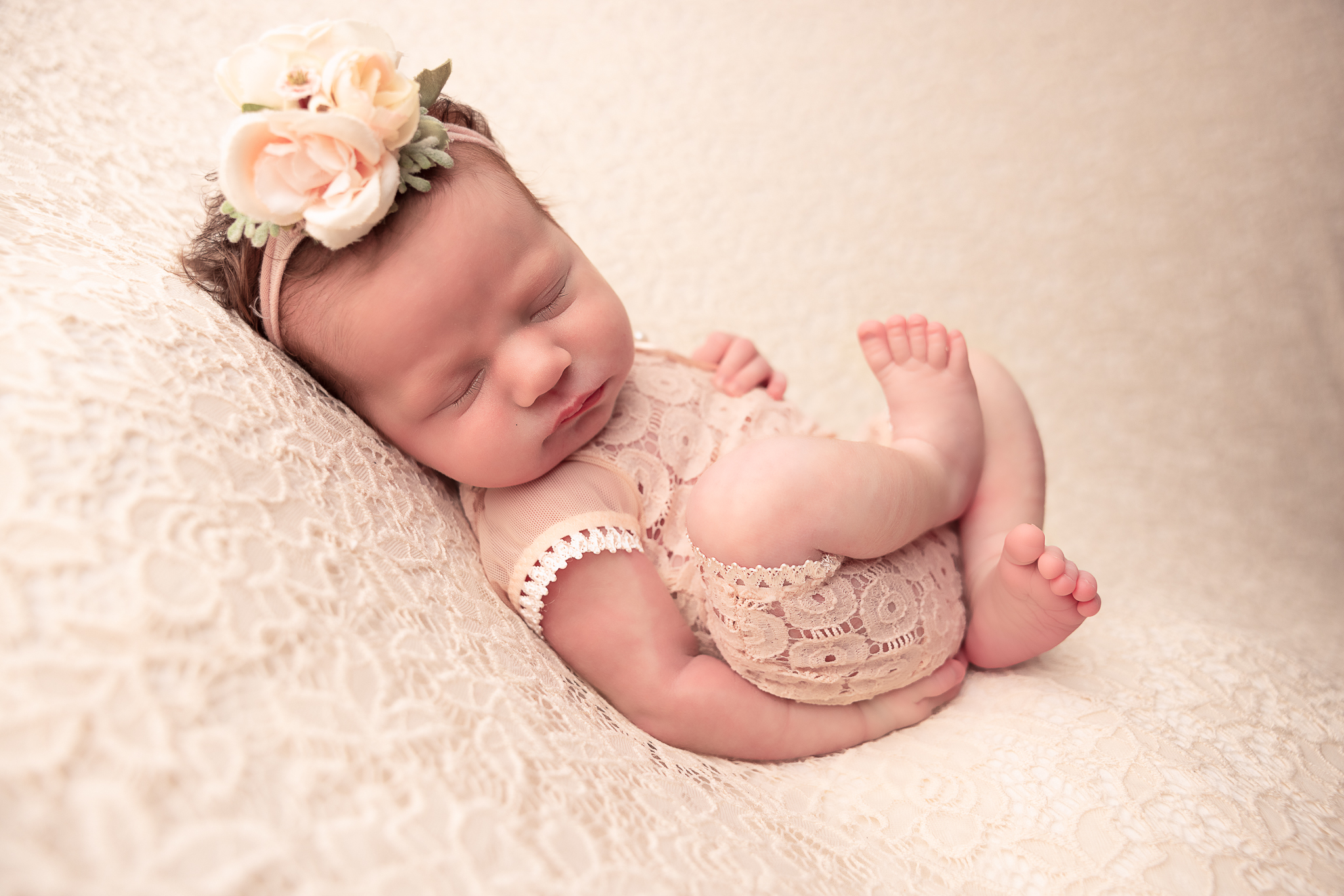 Baby laying on her back with crossed legs on lace backdrop and wearing a pink outfit