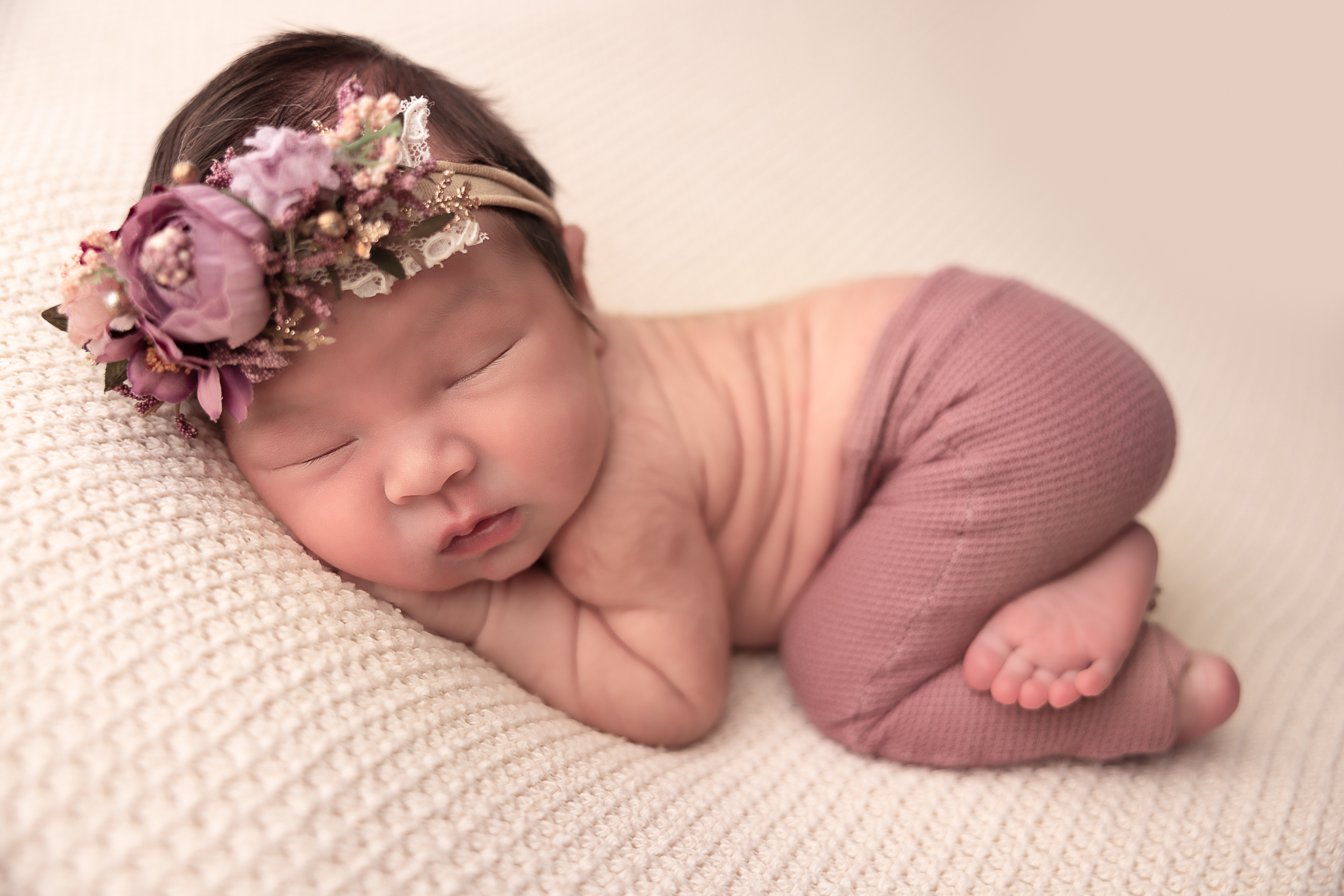 Baby with bum up wearing mauve pants and floral headband