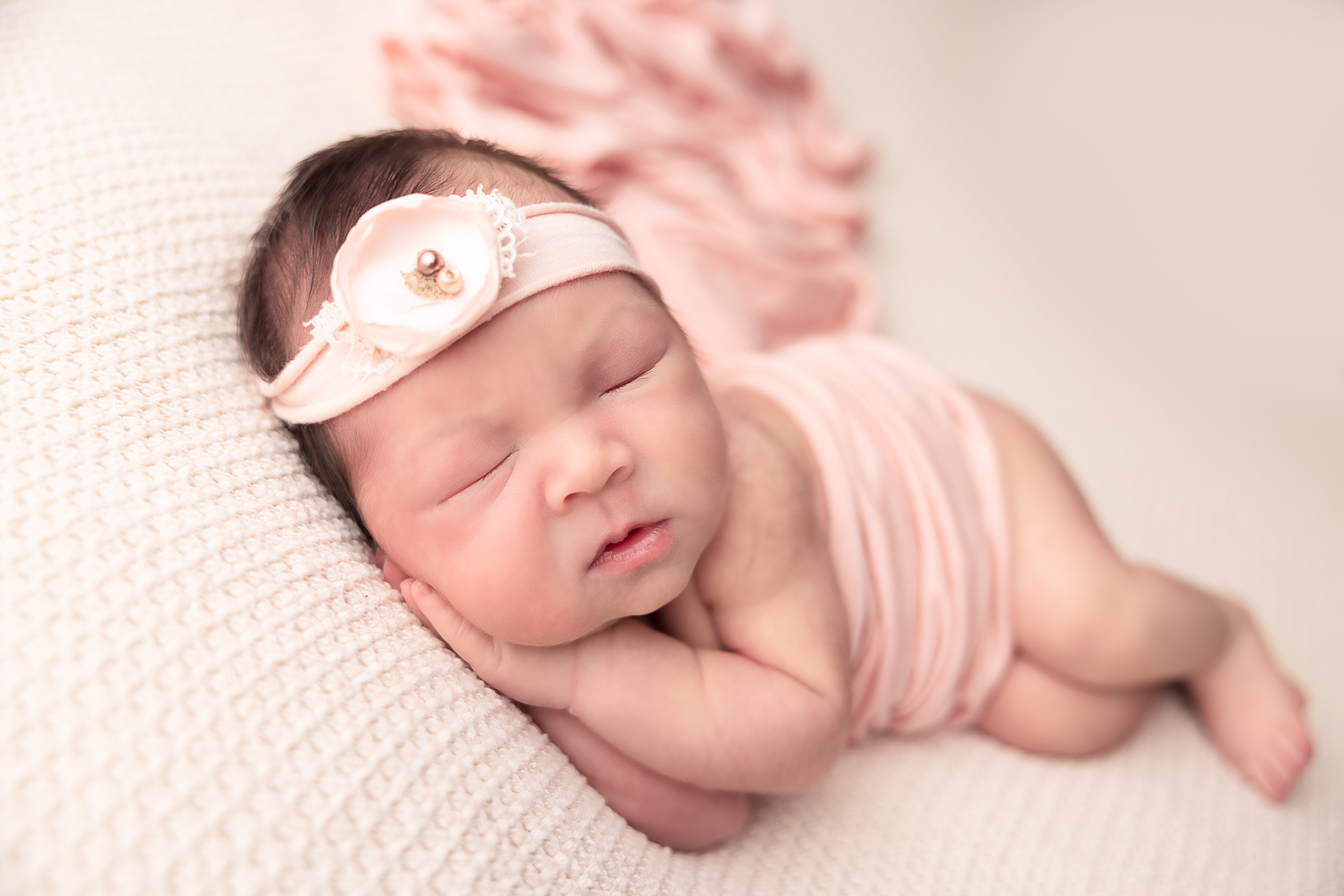 Side laying pose of baby wearing light pink headband and wrap across her body