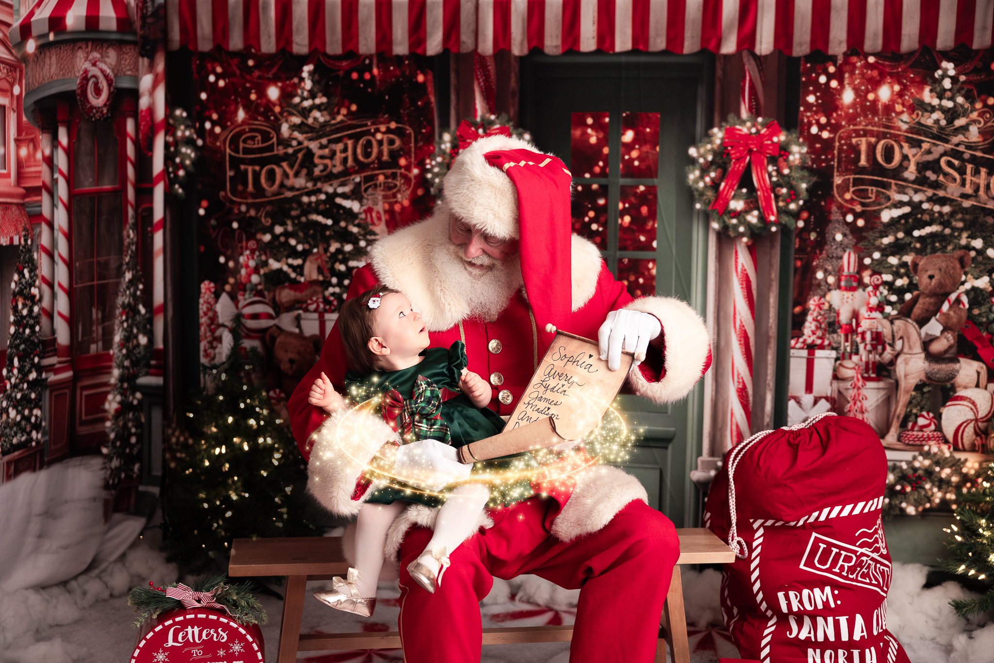 Santa holding a baby who is looking up at him while he's holding the scroll of the nice list