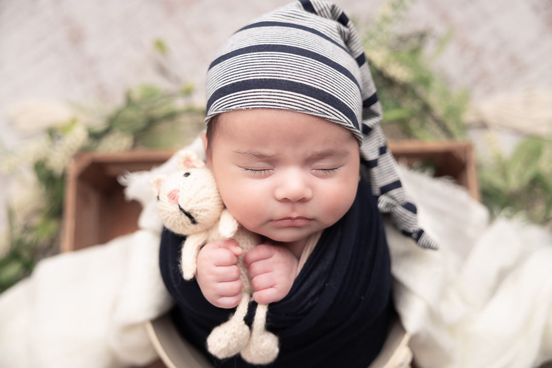 Baby Boy holding a lovey and wearing a blue and white striped hat