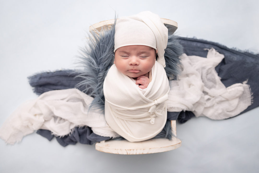 baby boy in a white crib prop with blue flokati and white layers