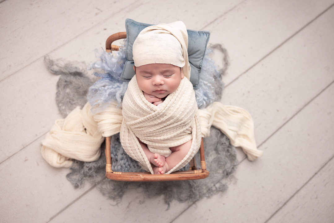 baby boy wrapped in cream with cream hat and blue pillow and layers