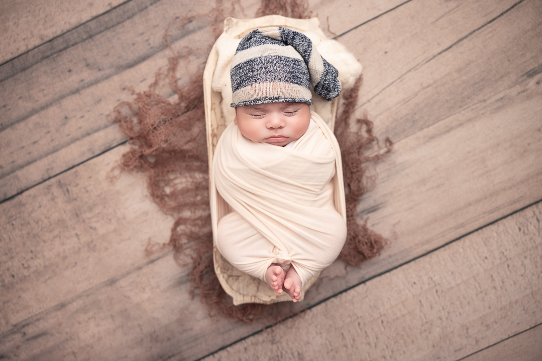 baby boy wrapped in cream with toes popping out wearing a blue and white striped hat