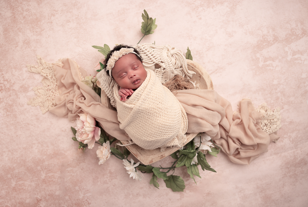 Baby in a heart shaped prop with pinks and florals baby is wrapped in cream wearing a headband