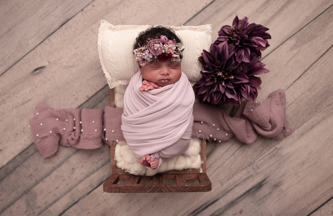 Baby in a tiny wooden baby bed in a purple wrap with dark purple florals