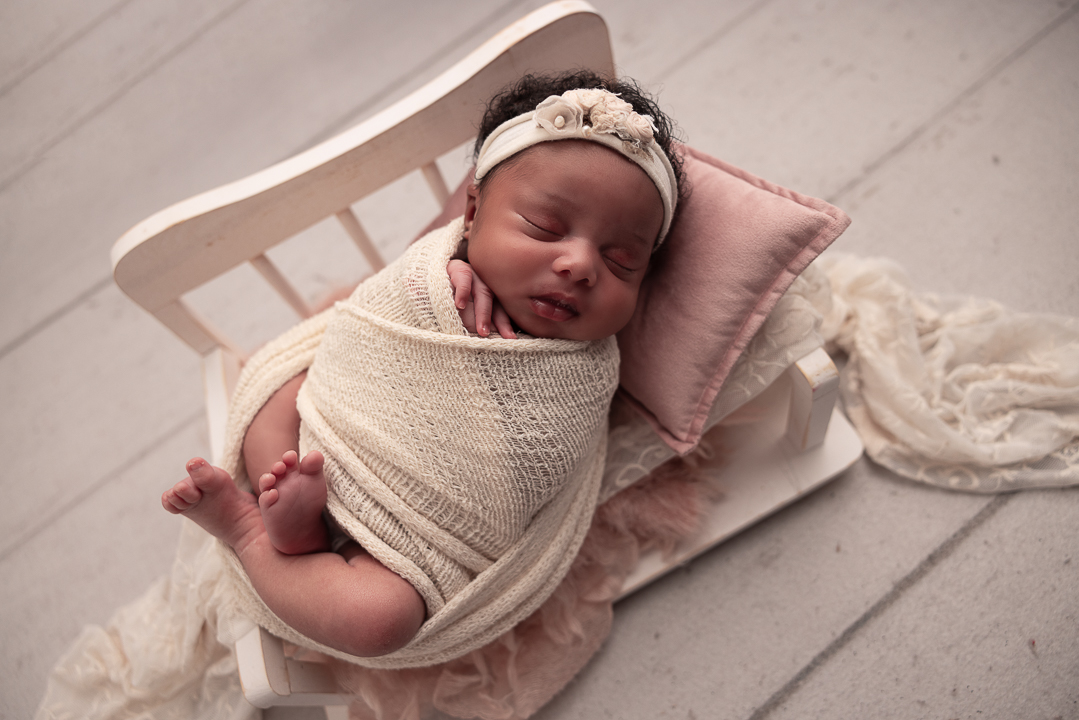 baby wrapped in a tiny white baby bed with her head on a pink pillow