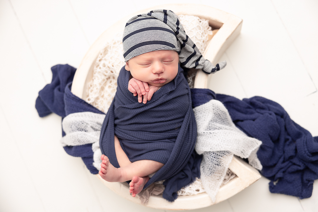 Baby in a moon prop wrapped in navy blue with striped hat