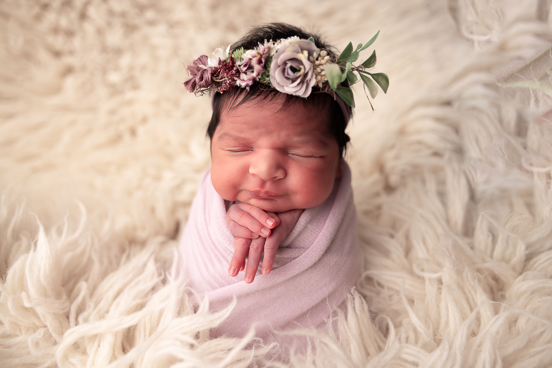 Newborn baby girl wrapped in purple wearing a floral headband
