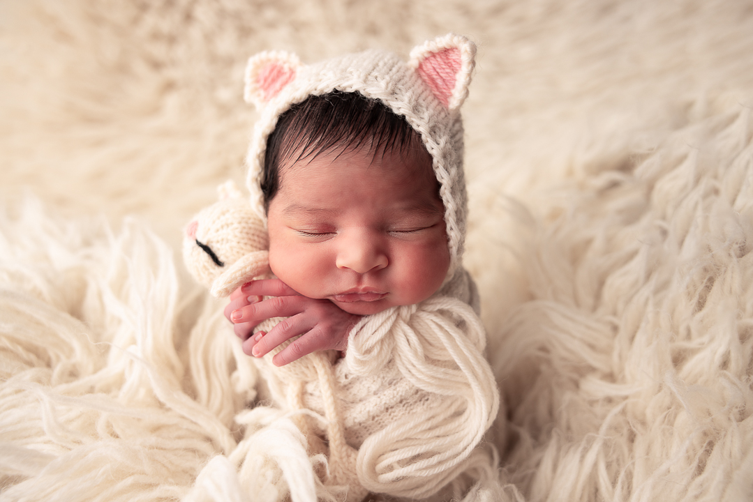 Newborn baby wrapped in white with a kitten bonnet holding a kitten lovey