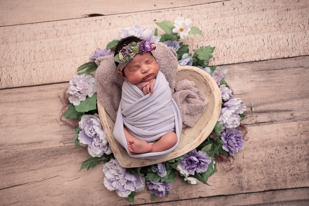 baby in a heart shaped prop with purple florals surrounding her