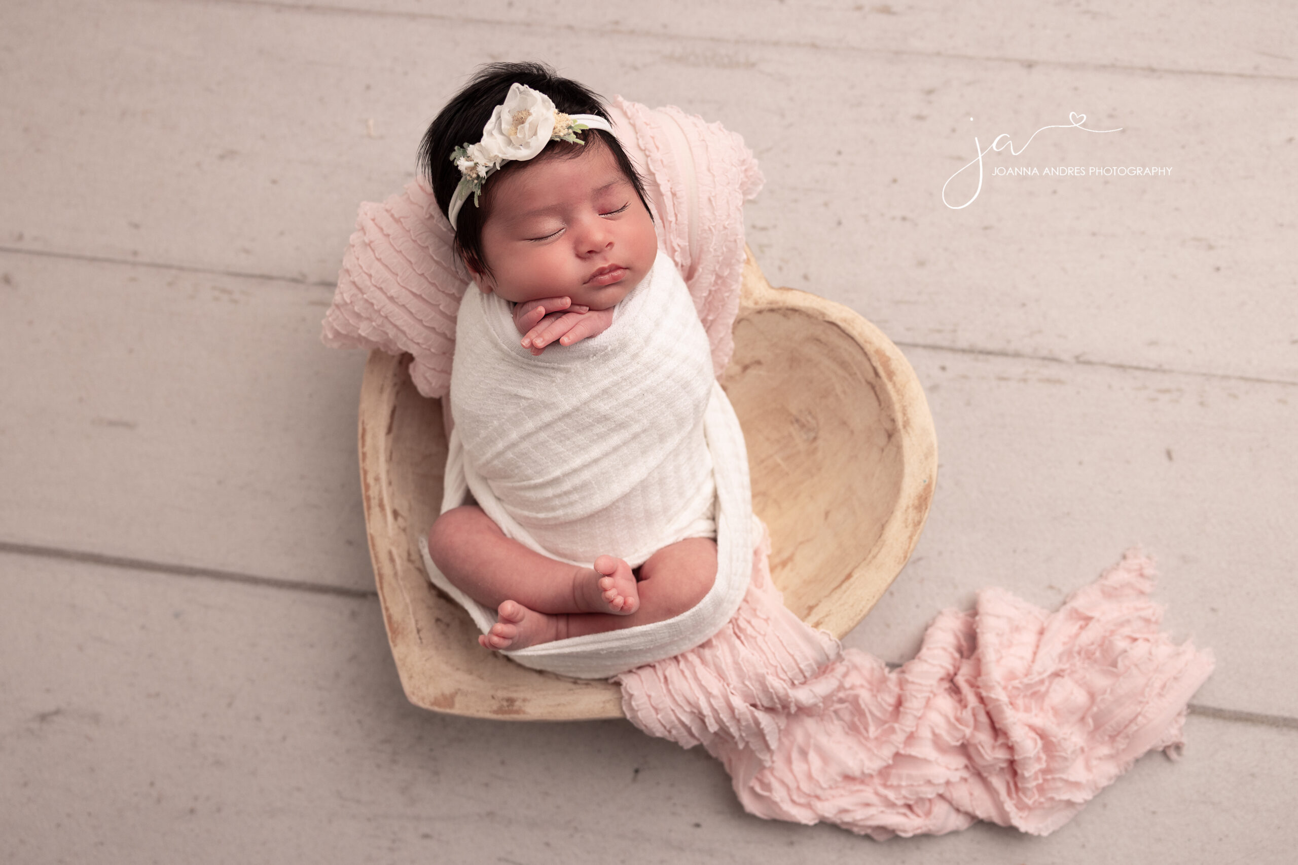Baby wrapped in white in a heart shaped prop with a pink layer