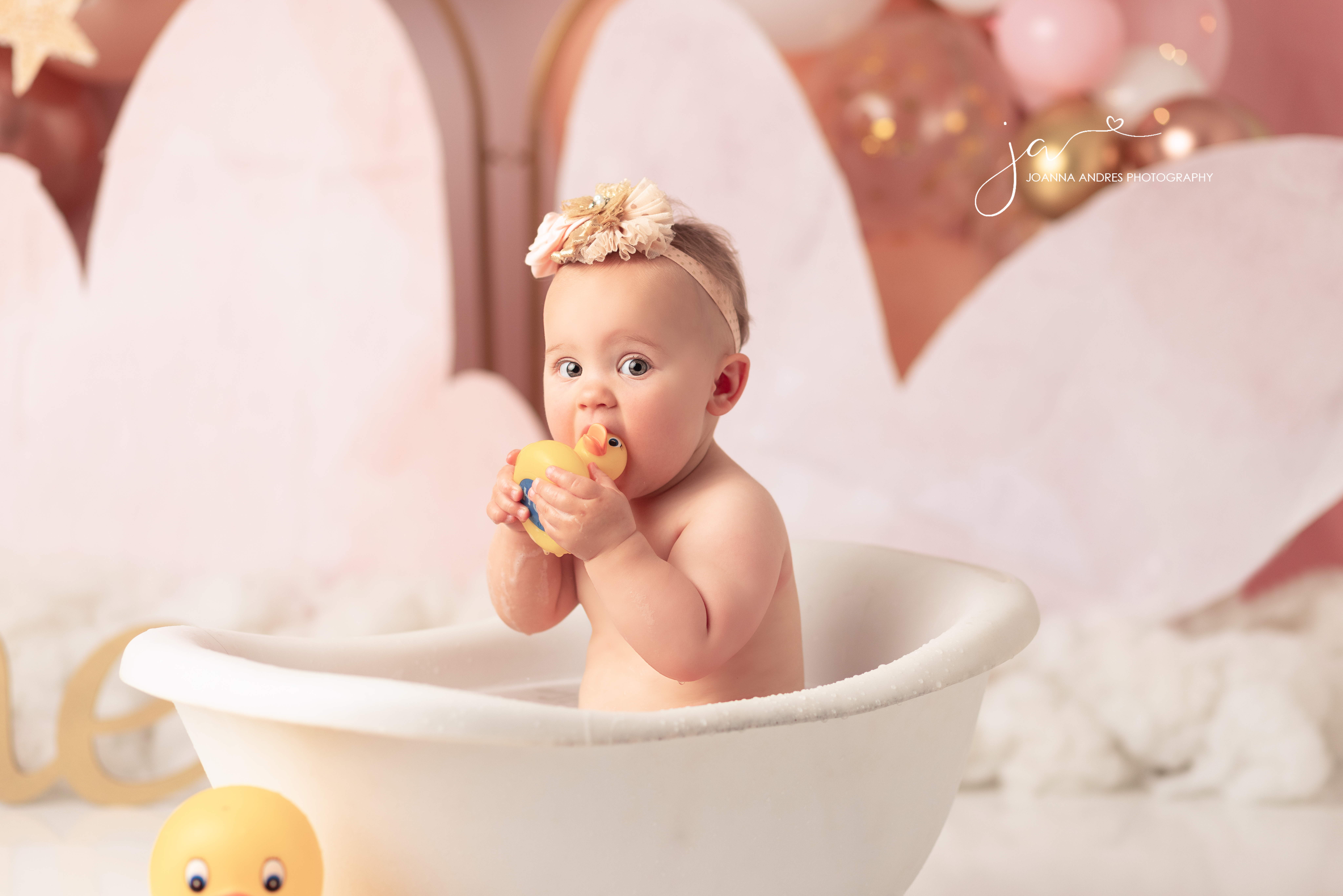 Baby in bathtub wtih rubber ducky in mouth